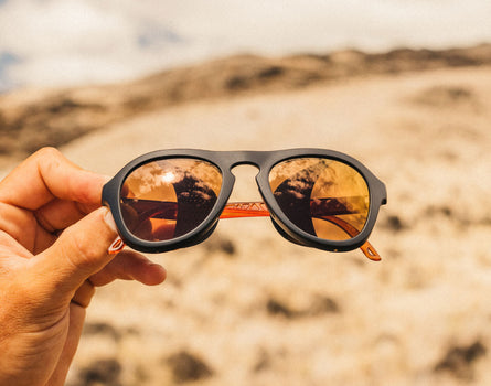 Sunglasses with reflective lenses held by a hand against a desert background
