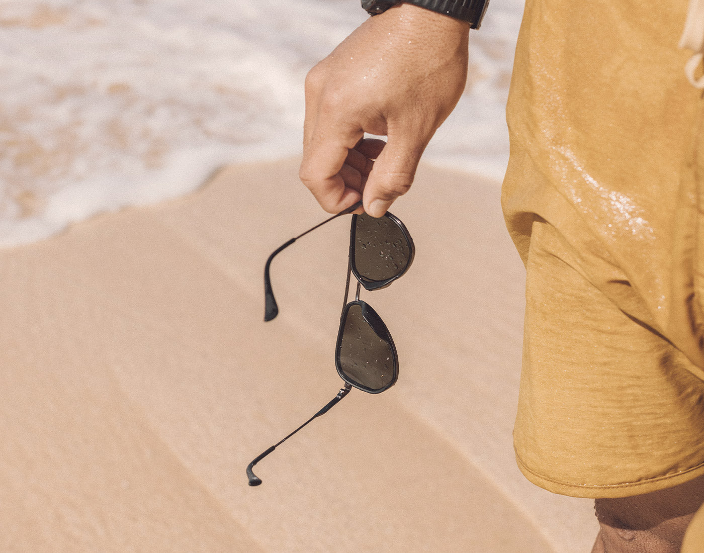hand holding sunski astra sunglasses on the beach