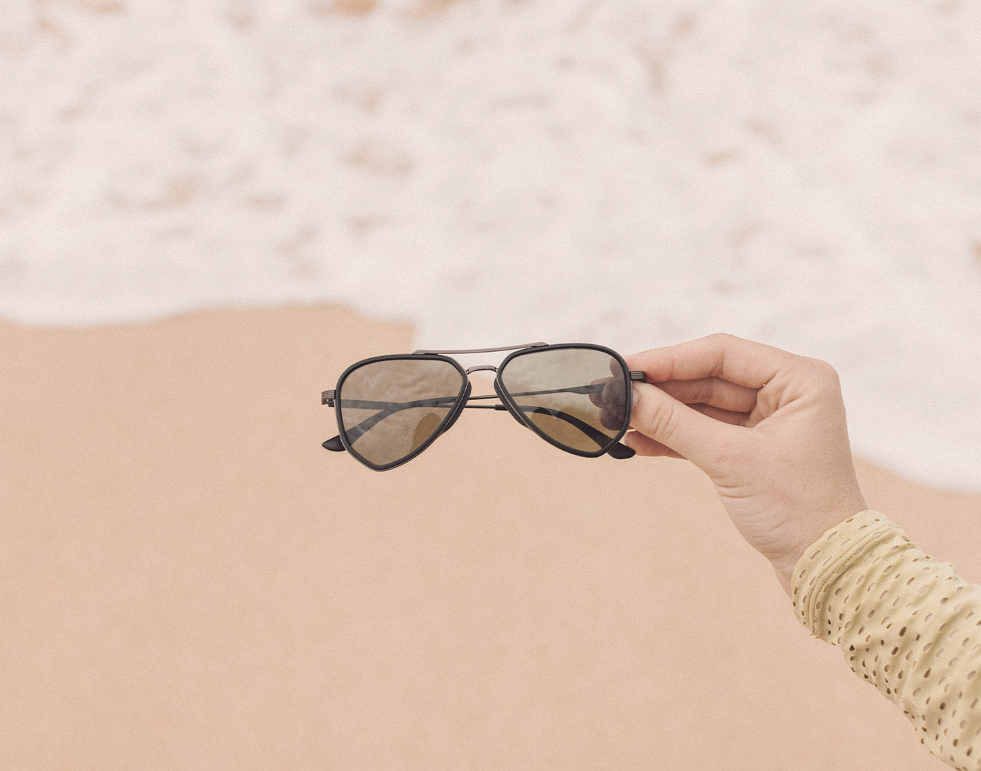 hand holding sunski astra sunglasses on the sand