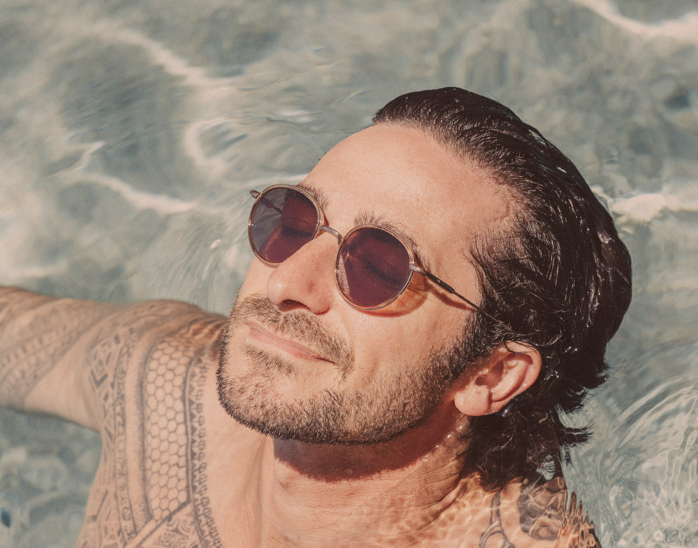 man floating in a pool wearing sunski baia sunglasses