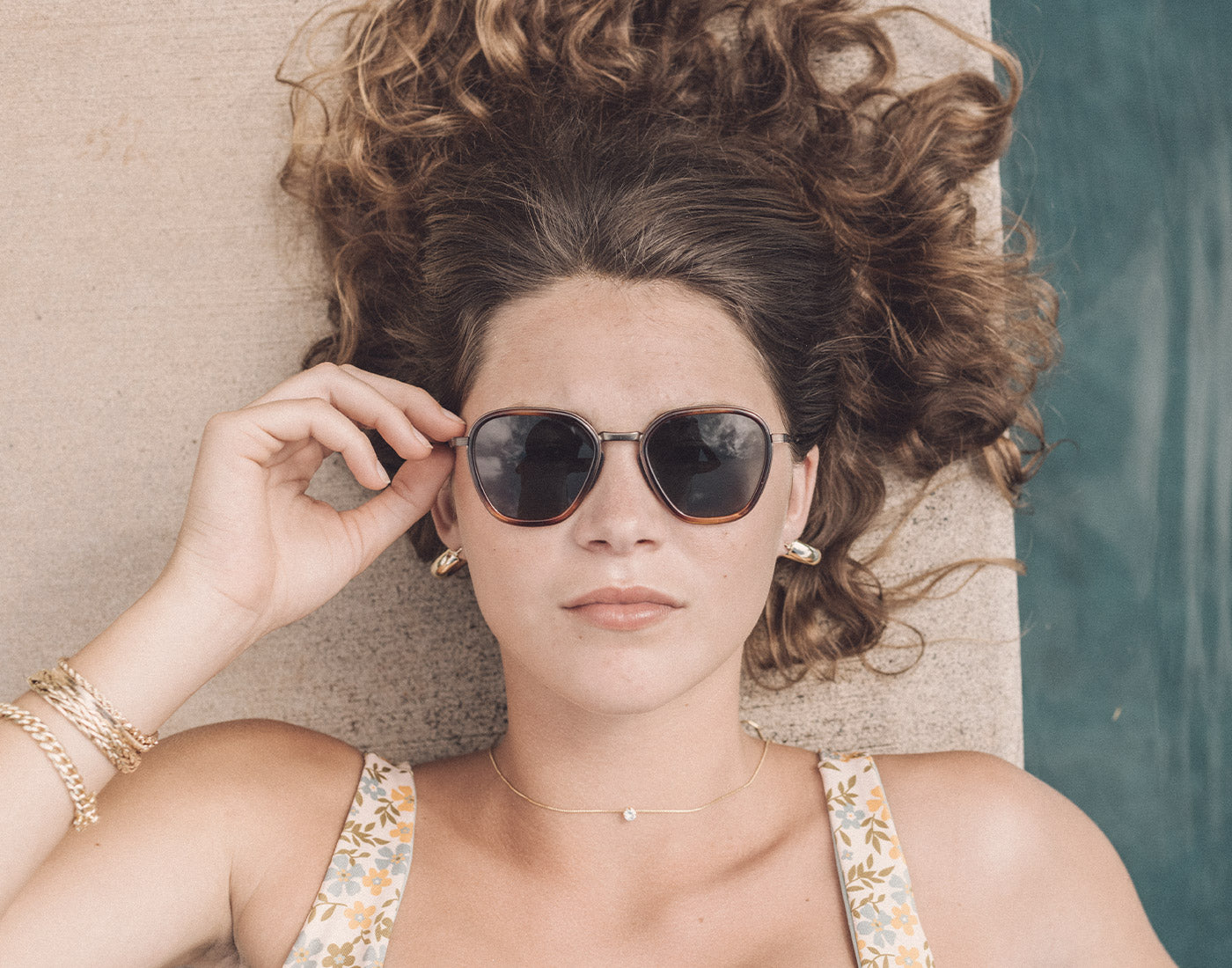 girl laying by pool looking straight wearing sunski bernina sunglasses
