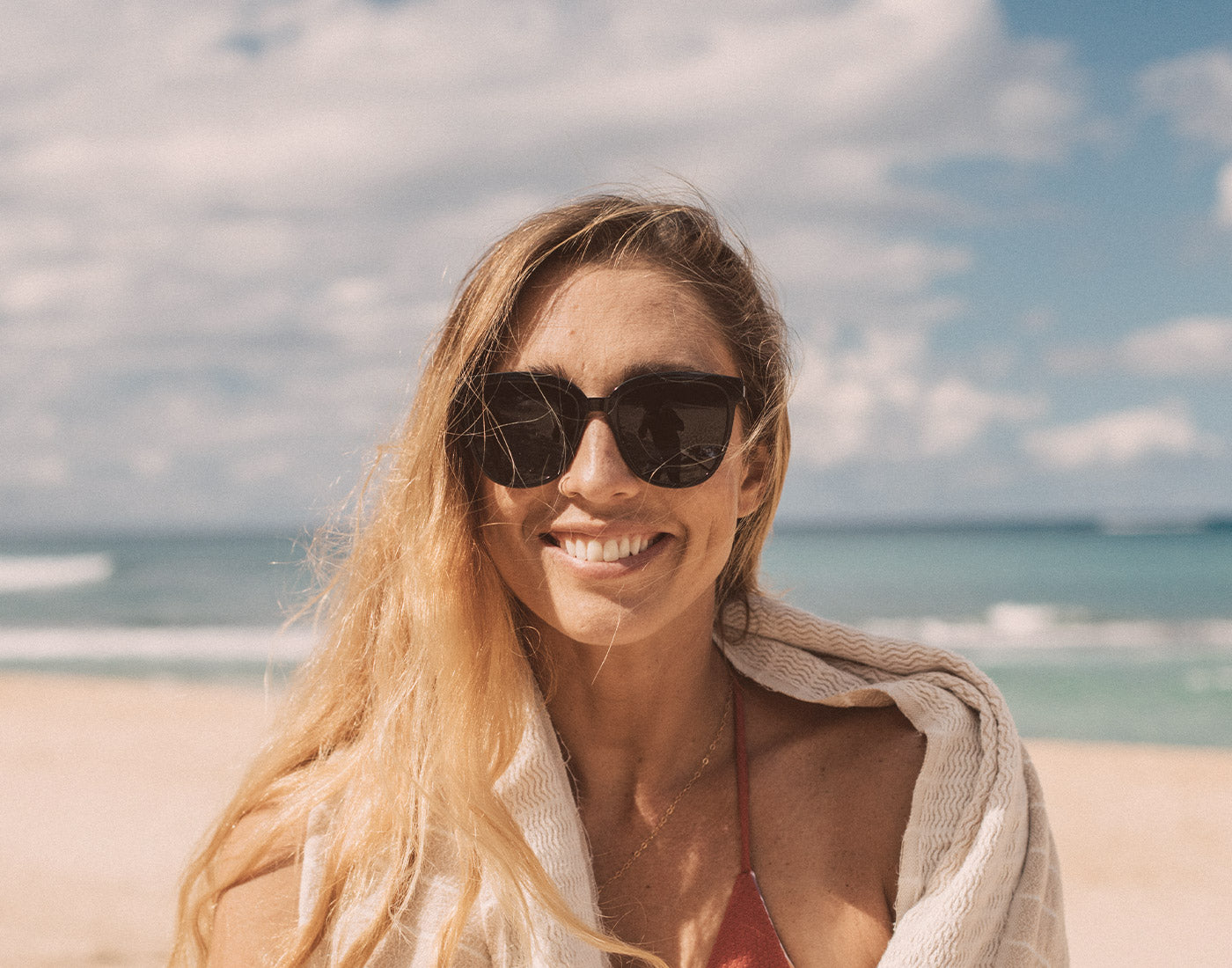 girl wrapped in towel at the beach wearing sunski camina sunglasses