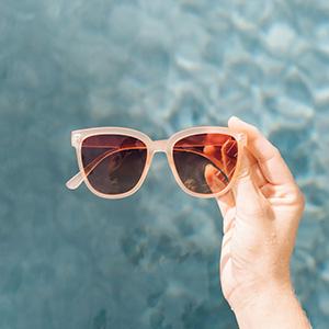 hand holding sunski camina sunglasses in front of water