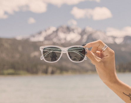 hand holding sunski headland sunglasses in front of the mountains