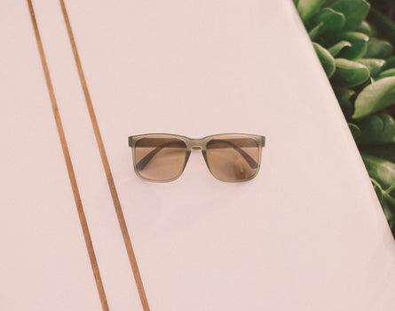 sunski kiva sunglasses laying on a surfboard