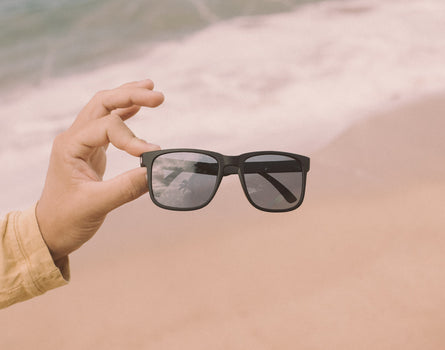 hand holding sunski kiva sunglasses on the beach