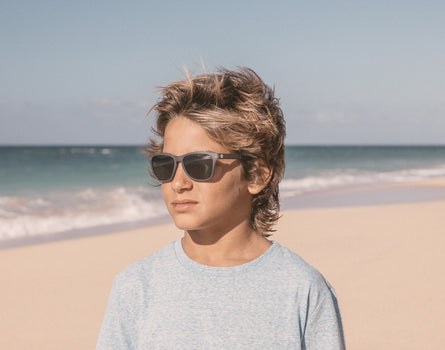boy on the beach in the wind wearing sunski mini headland sunglasses