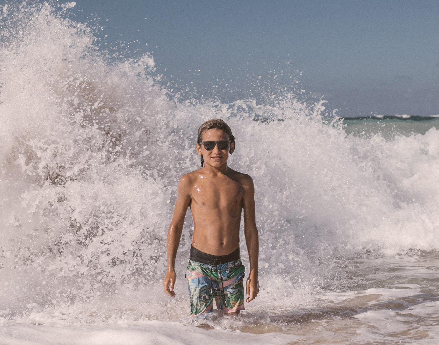 boy in the waves wearing sunski mini headland sunglasses
