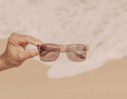 hand holding sunski puerto sunglasses over sand