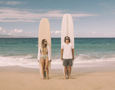 guy and girl standing in front of surfboards wearing sunski puerto sunglasses