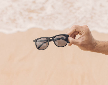 hand holding sunski seacliff sunglasses over sand