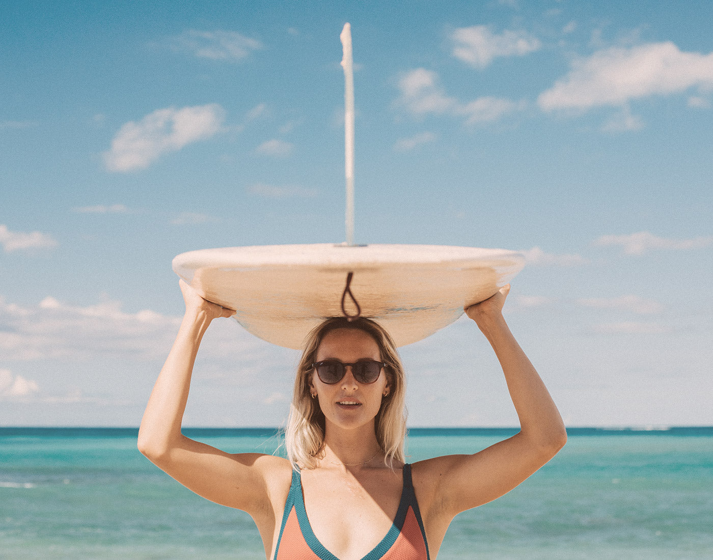 girl holding surfboard over head wearing sunsk yuba sunglasses