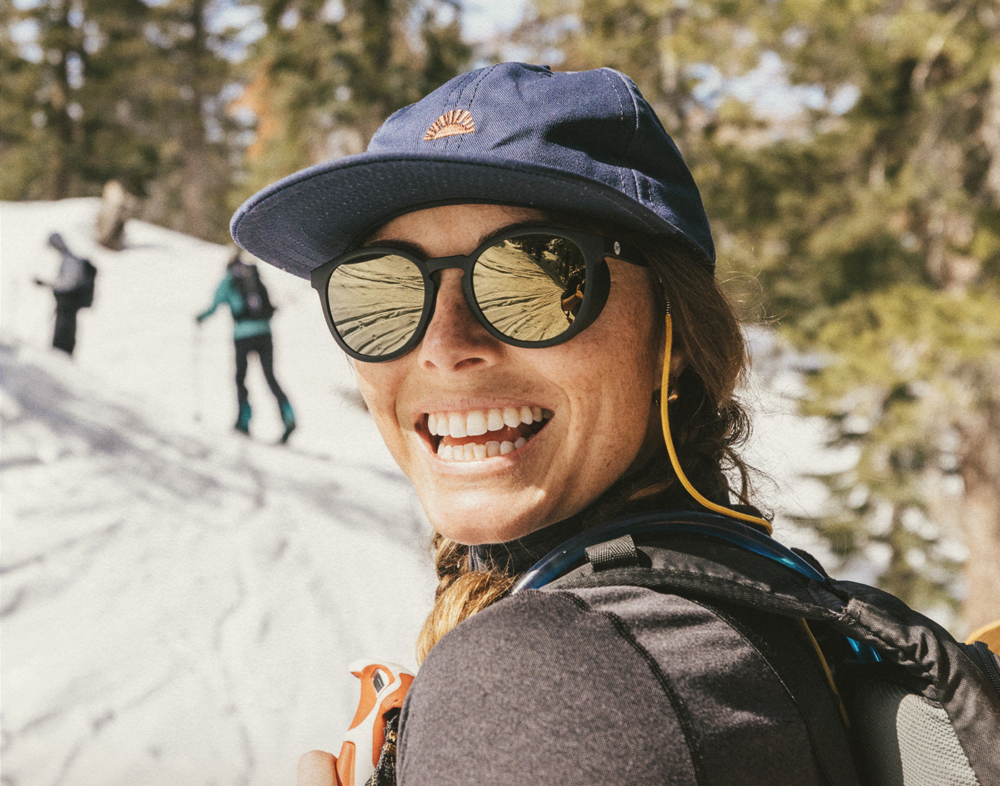 girl on a mountain smiling wearing sunski sunburst hat